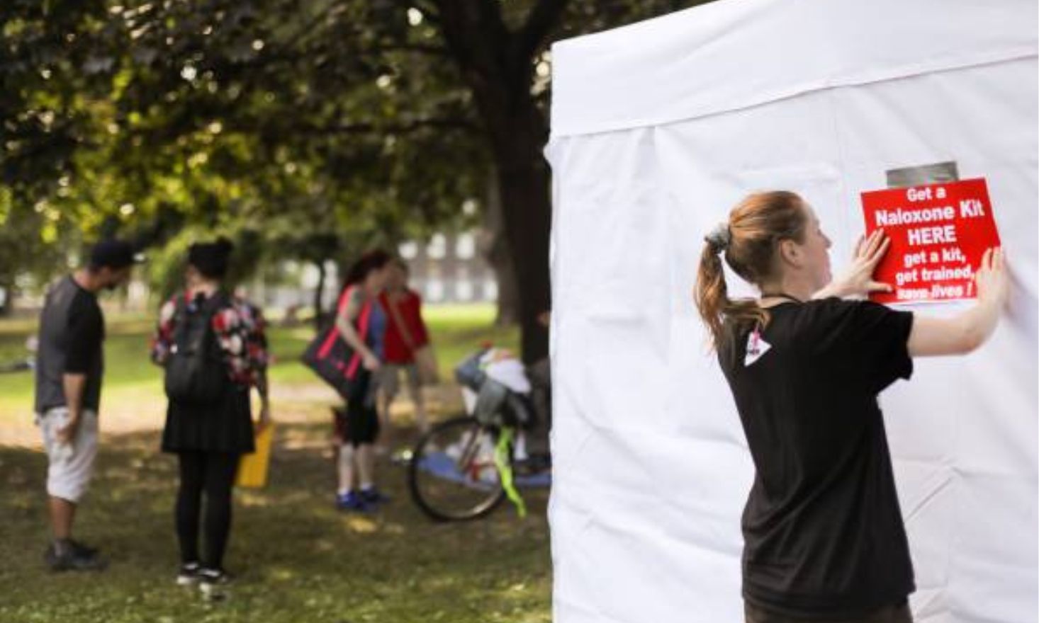 A person putting up a sign that reads "Get a Naloxone kit HERE"