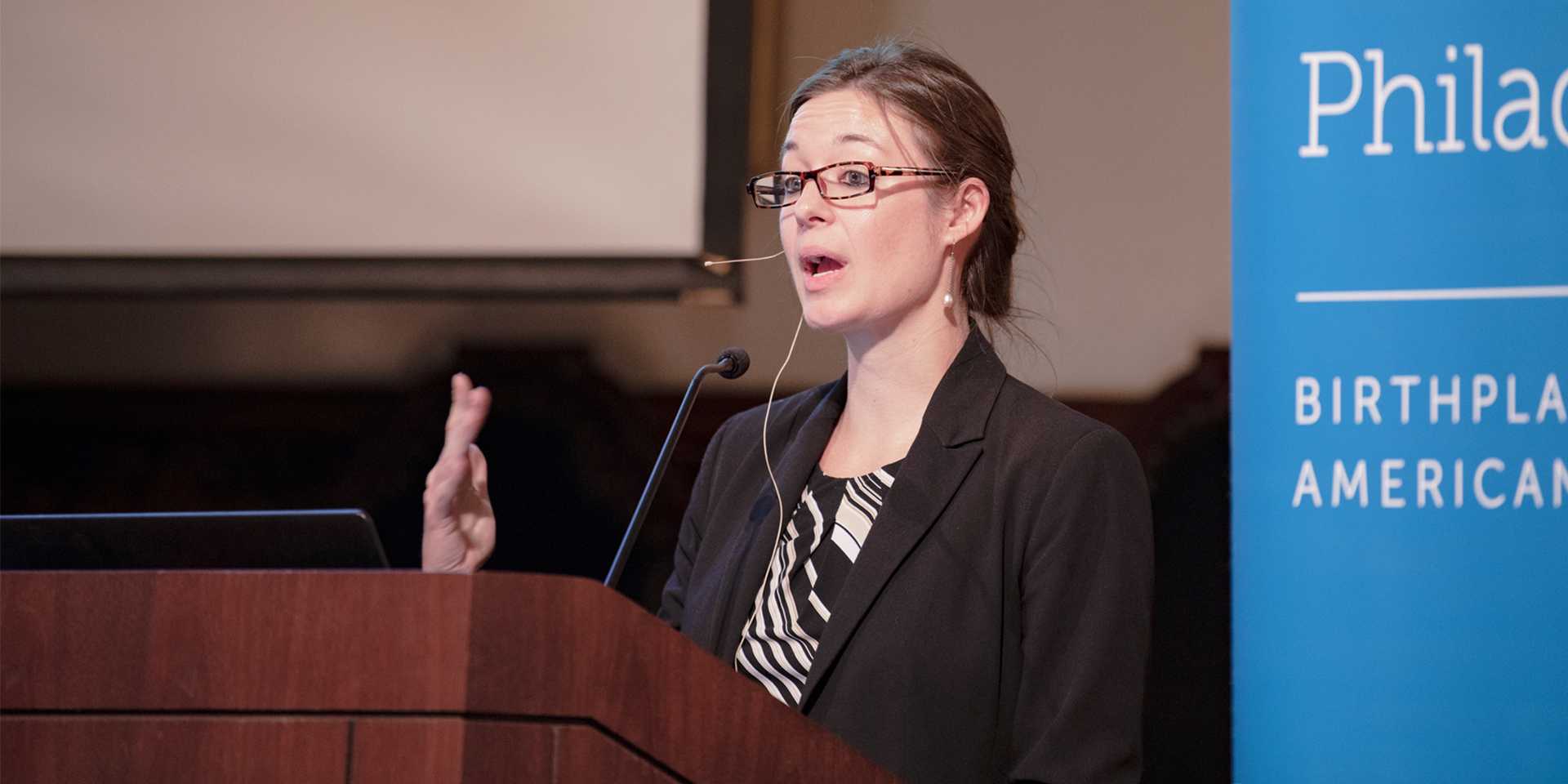 Woman in black blazer speaking at podium