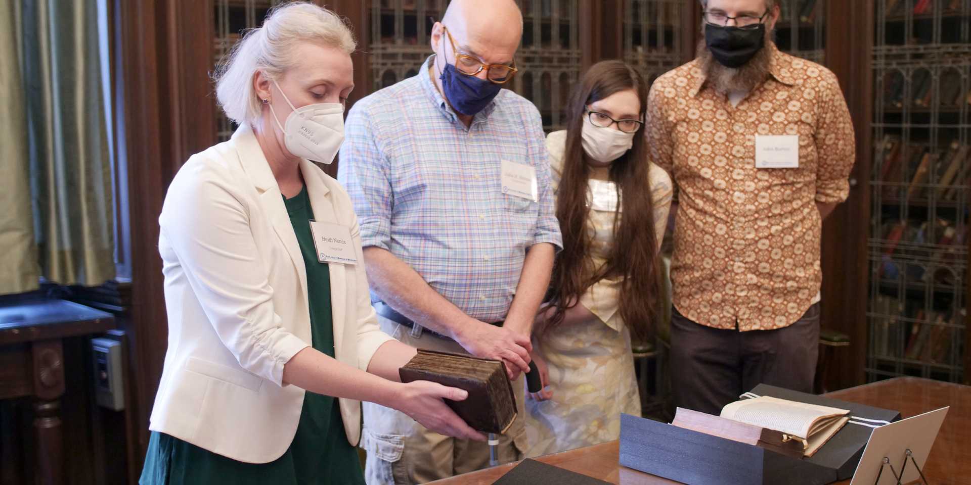 Librarian holding antique book while three others look on